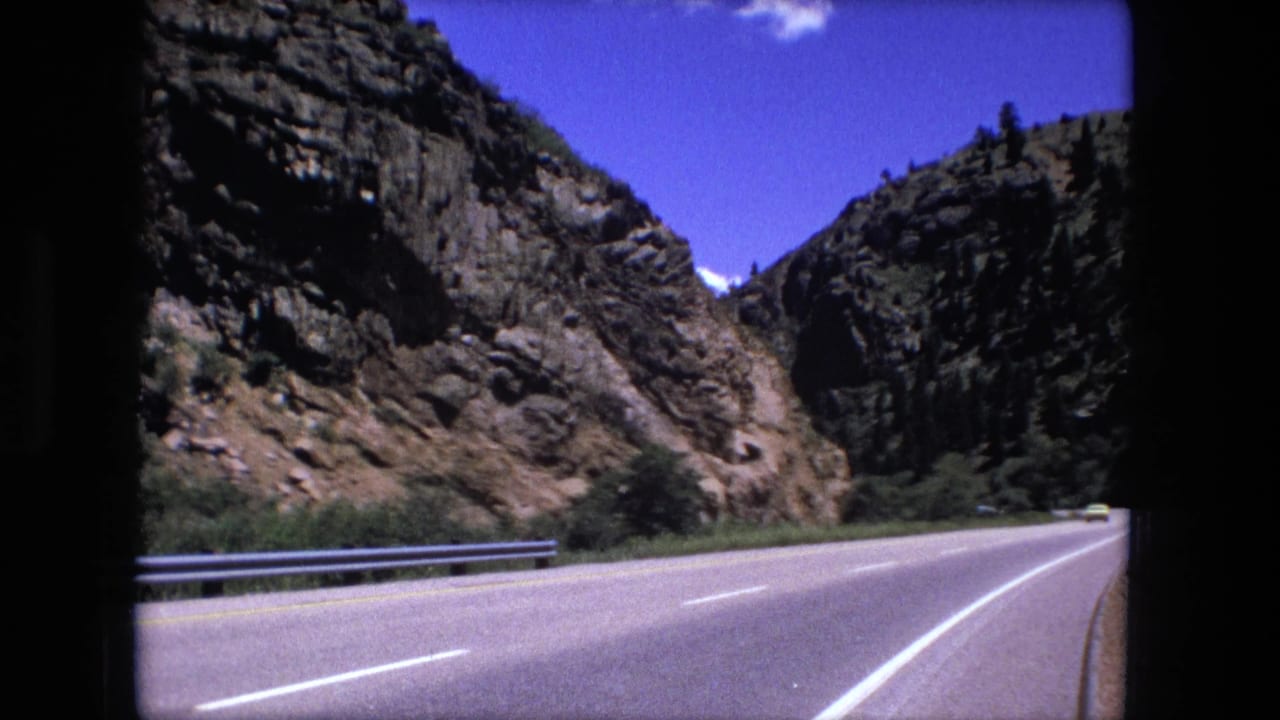 Highway stretching toward steep rocky slopes with a distant yellow vehicle.