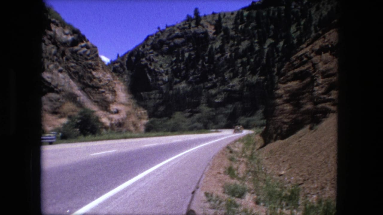 Curving two-lane road beside rocky cliffs under a blue sky.