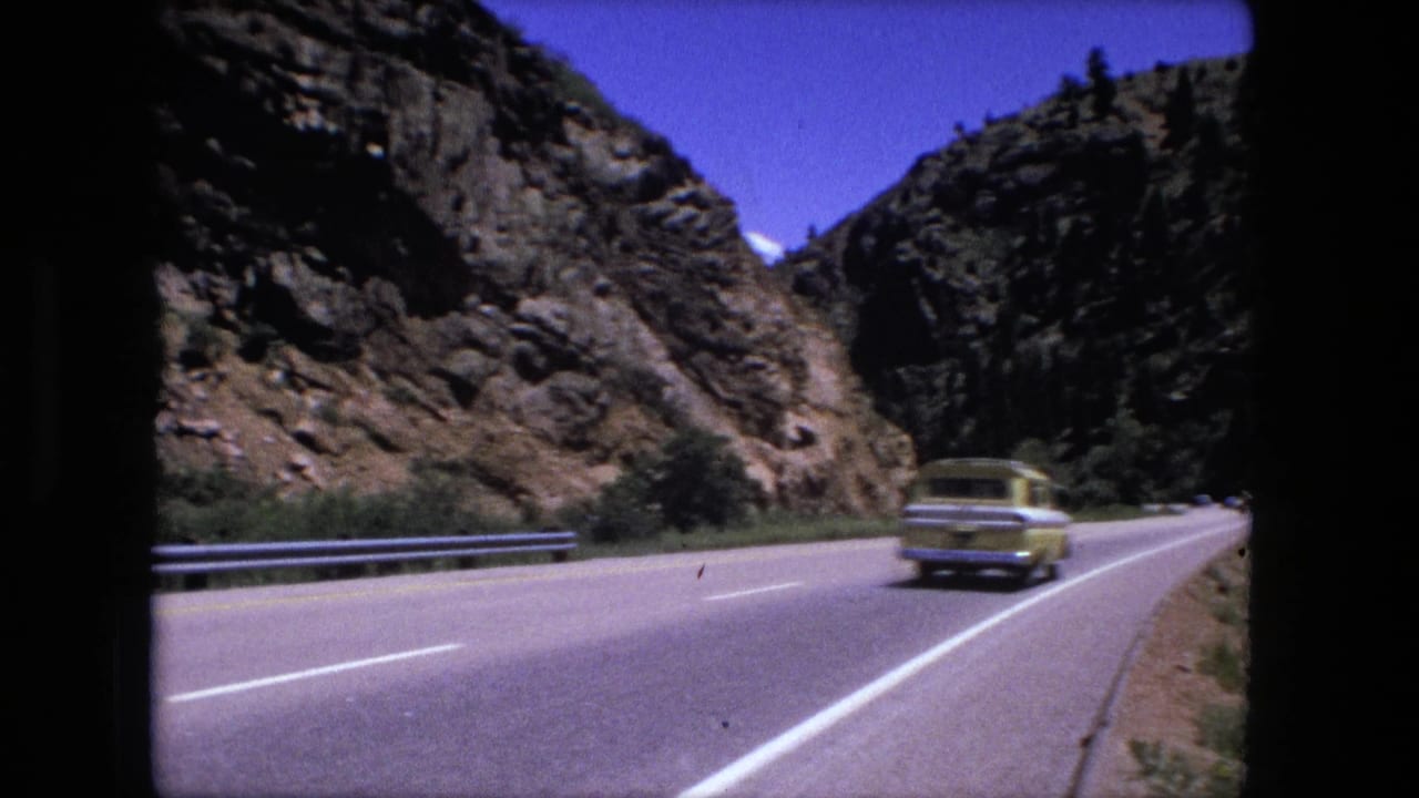 Yellow station wagon driving on a mountain road near rocky cliffs.