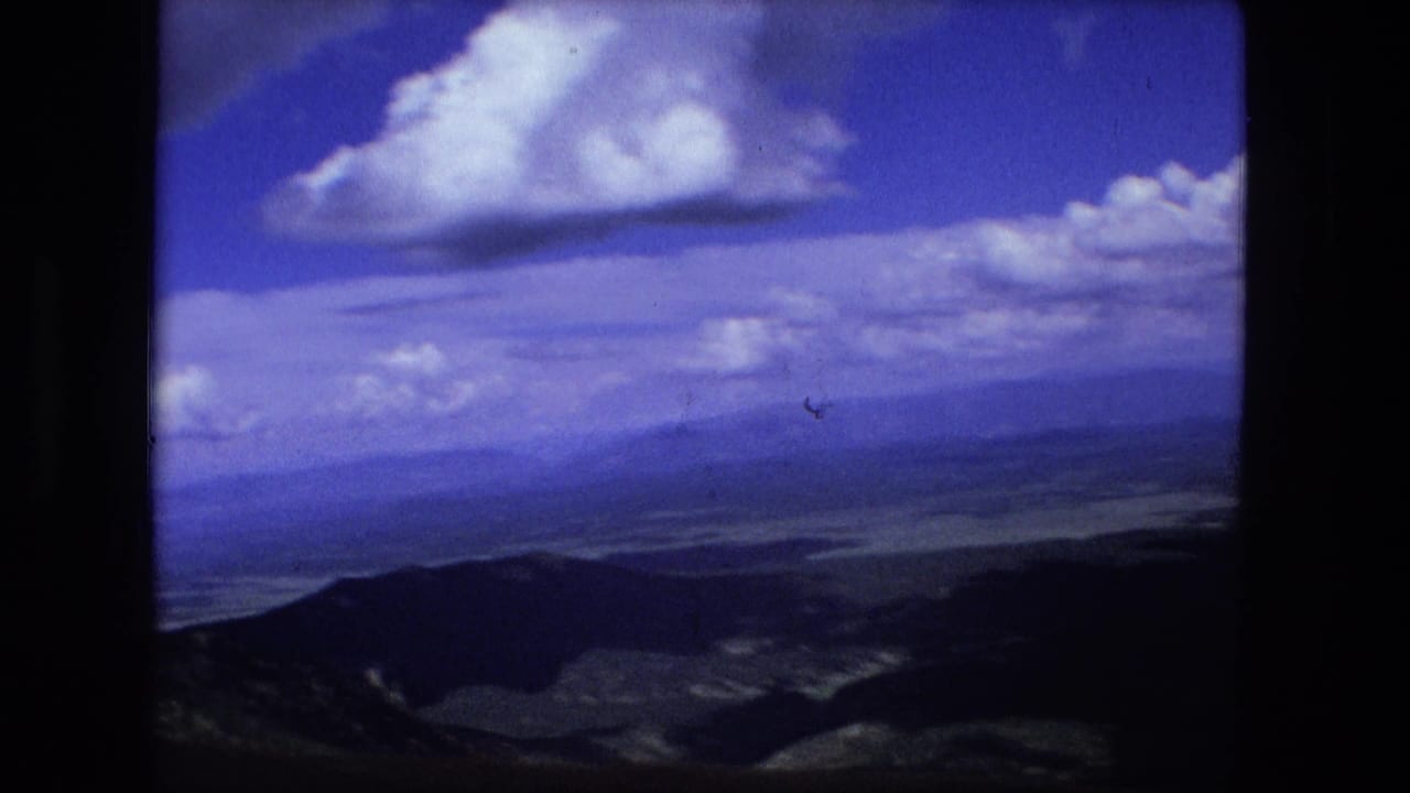 Mountain landscape seen from above with clouds and hazy distant terrain.