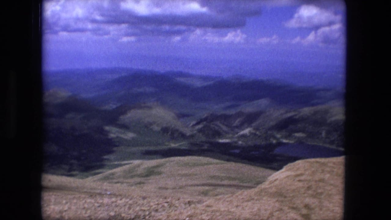 Mountain ridges and golden foreground slopes beneath a blue sky with scattered clouds.