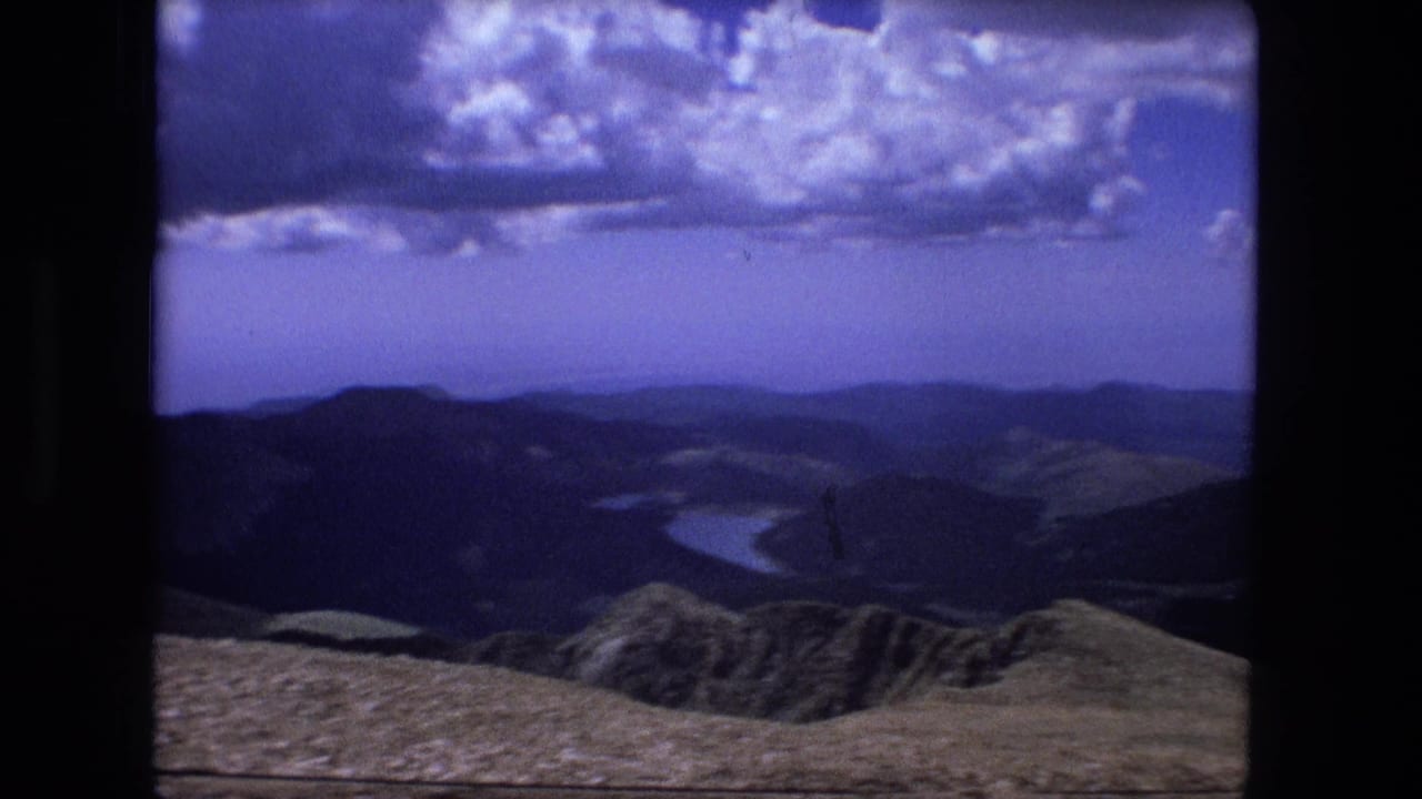 Mountain ridges under a blue sky with clouds and distant water below.