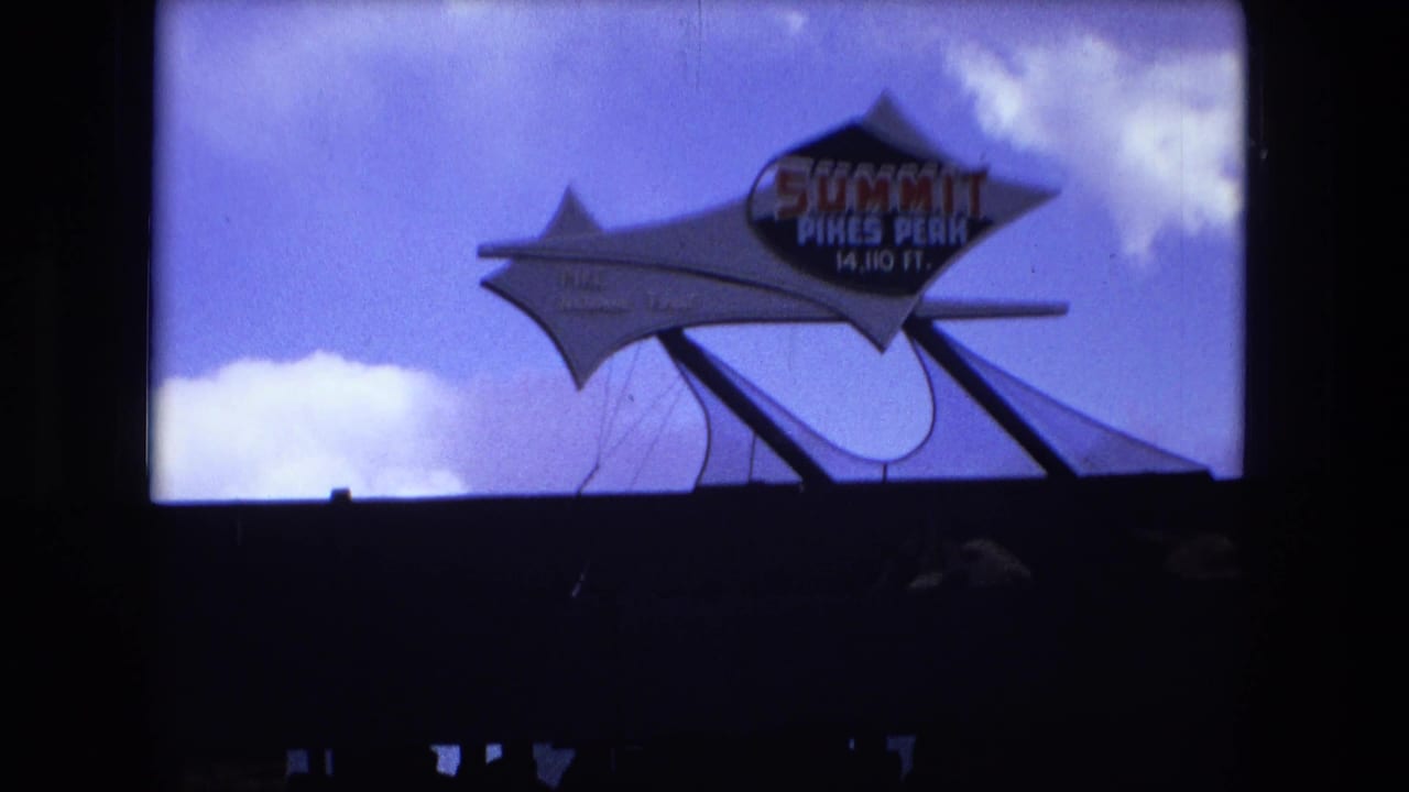Summit Pikes Peak sign against blue sky, partly framed by dark 8mm film borders.