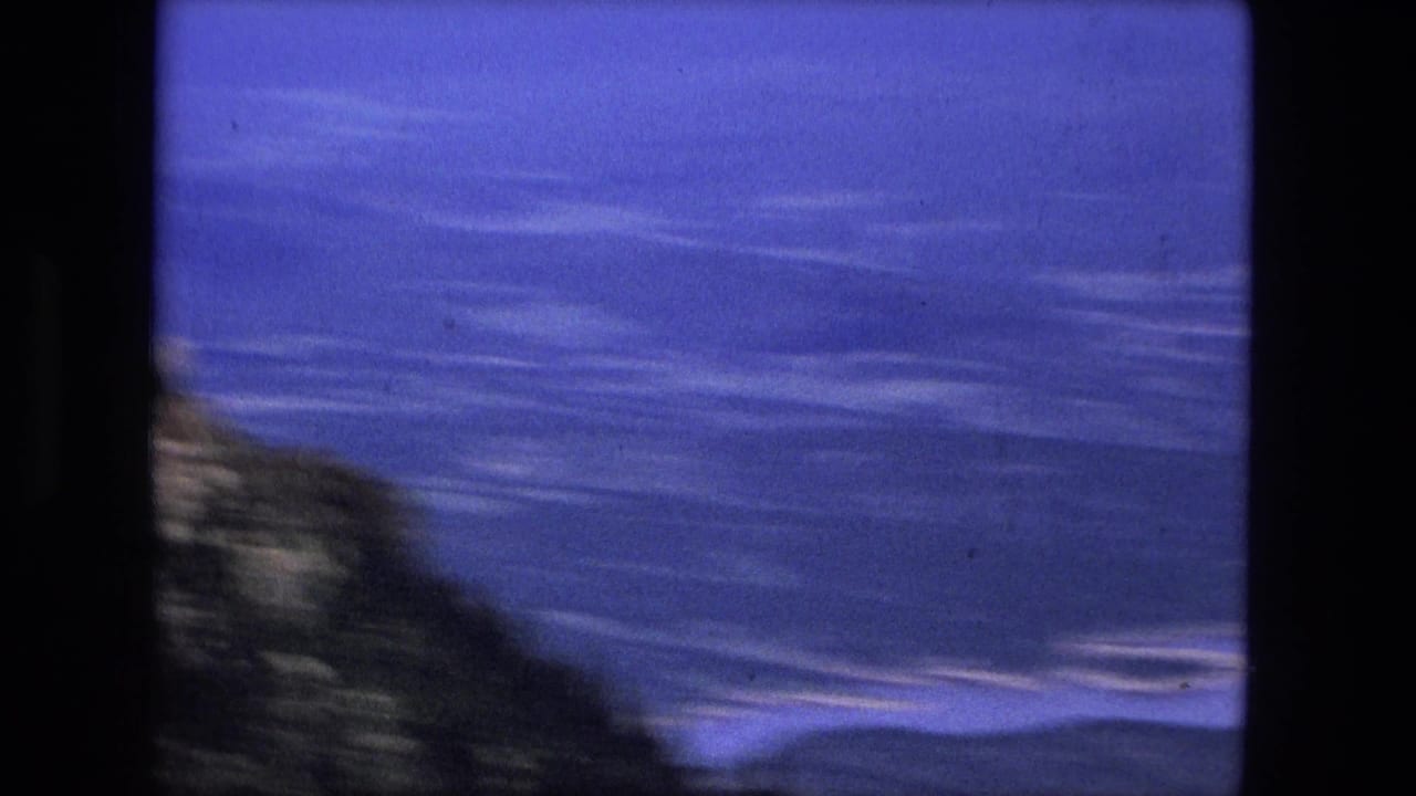 Blue mountain ridges and valley water seen through a dark 8mm film frame edge.