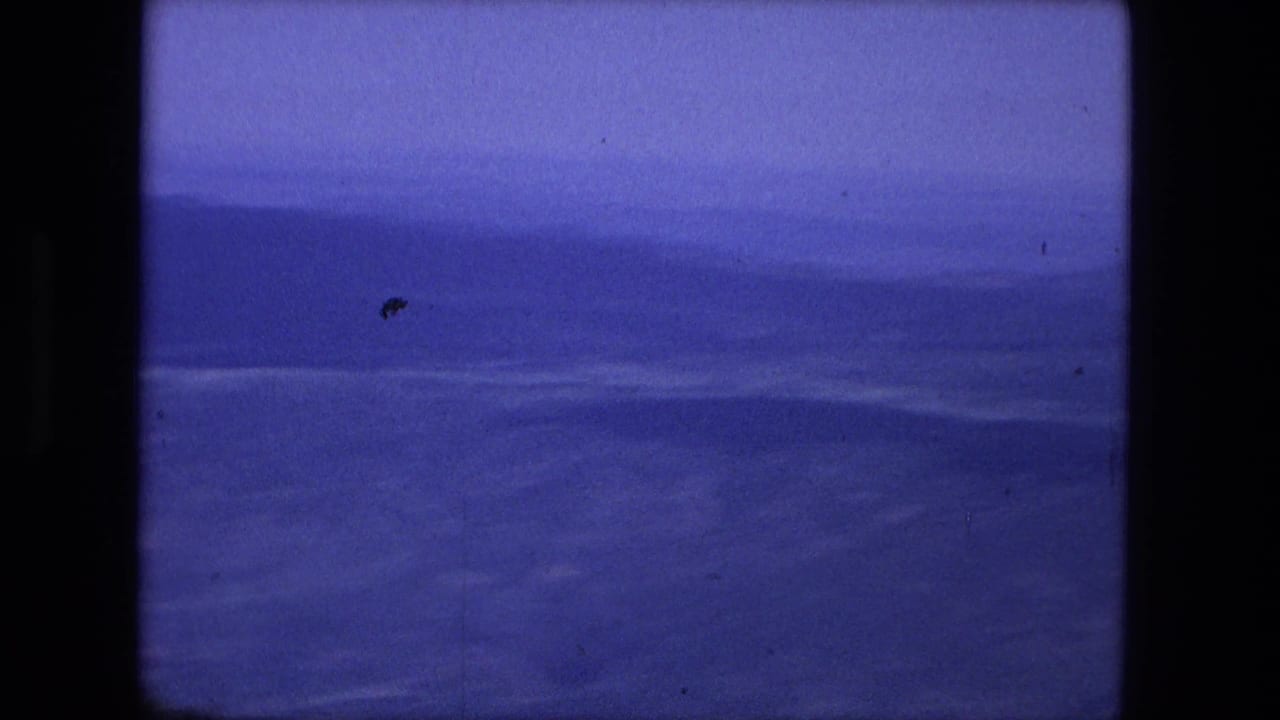 1976 8mm frame of a distant blue mountain range under a hazy sky, with visible dust and faded color.