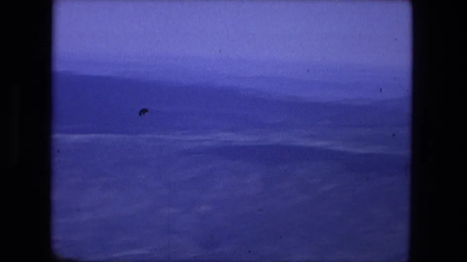 1976 8mm frame of a distant blue mountain range under a hazy sky, with visible dust and faded color.