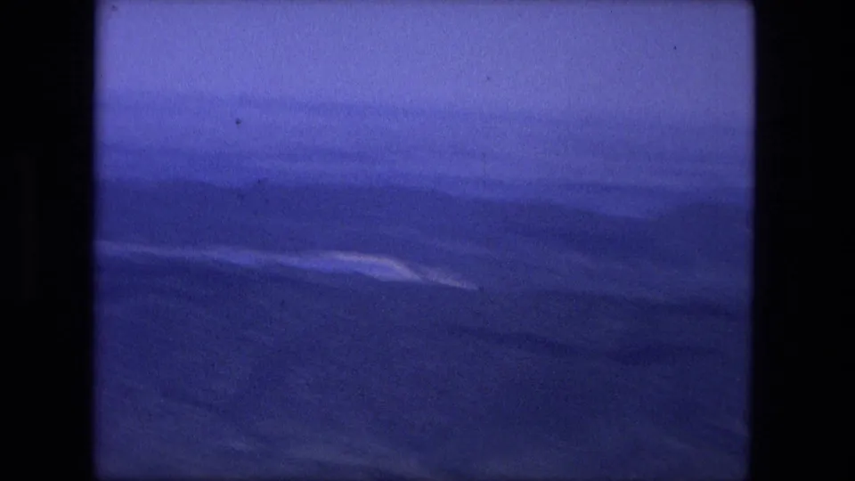 1976 8mm home-movie view across a blue-toned valley and layered mountain ridges, softened by haze and film fade.