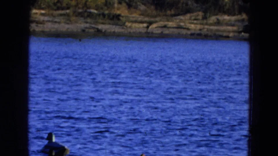 1968 8mm home-movie frame from Diller, Nebraska showing blue lake water, a far bank, and dark vertical film borders.
