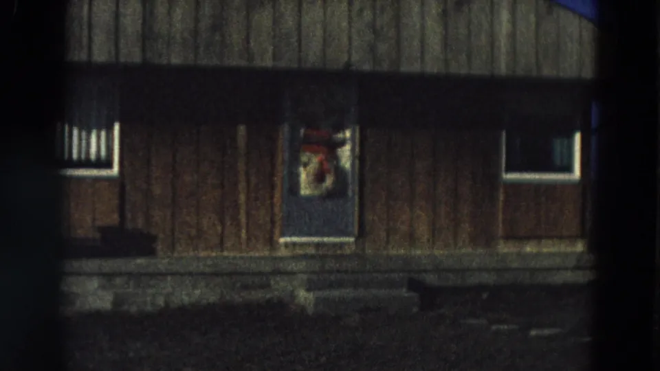 A rustic wooden house exterior in Diller, Nebraska, with small windows and a holiday decoration on the central door.
