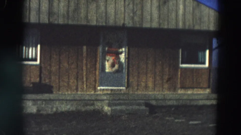 Closer 8mm view of the Diller house exterior, showing vertical siding, two windows, and a decorated door.