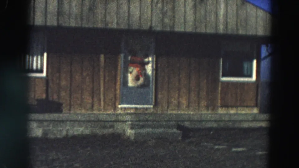 Handheld 1968 Diller, Nebraska footage holds on a wooden house facade with a decorated door and dark foreground yard.