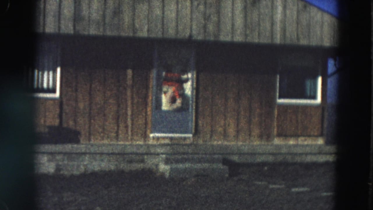 Wood-sided building with a blue door, small windows, and dark film-frame edges.