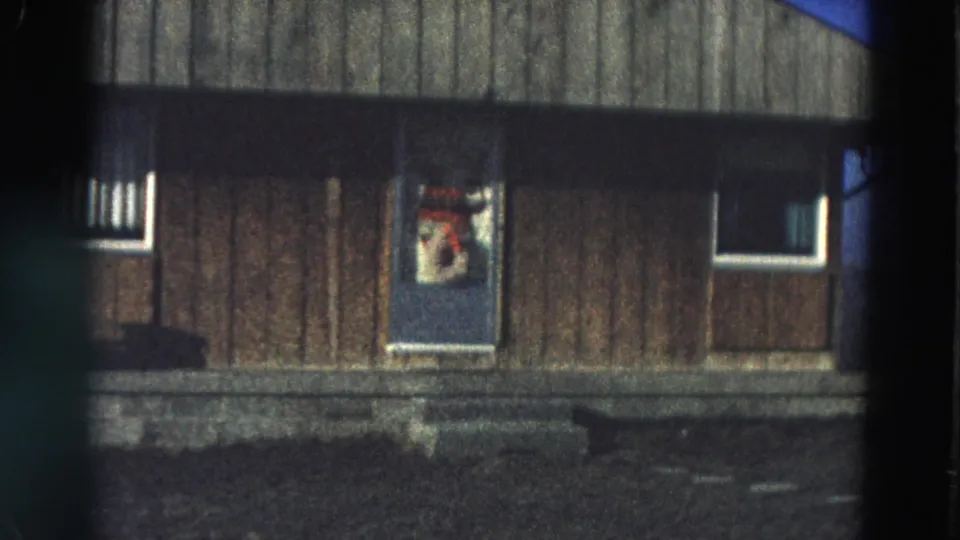 1968 Diller, Nebraska frame showing a wood-sided exterior with a blue door, small windows, and a decoration in the door glass.