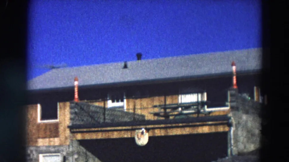 1968 Diller, Nebraska view of a wooden building with porch railing, picnic table, roof edge, chimney-like vents, and blue sky.
