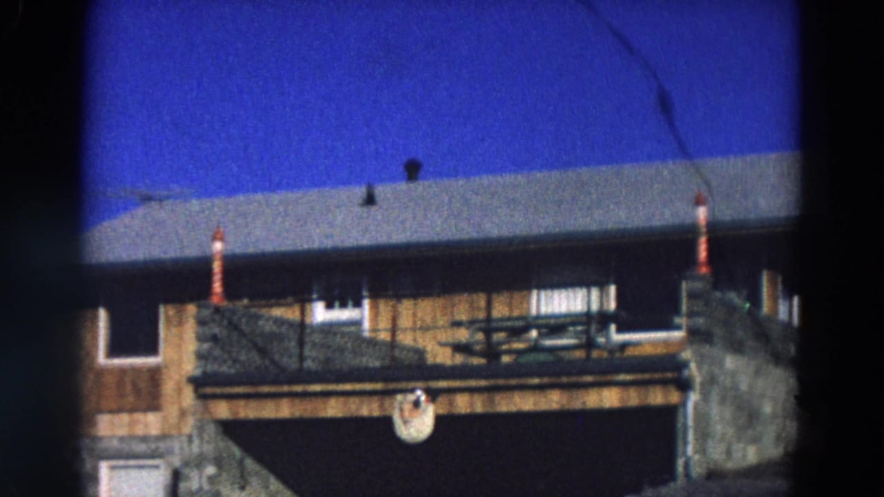 Two-story house exterior with wood siding, stone lower wall, porch rail, and blue sky.