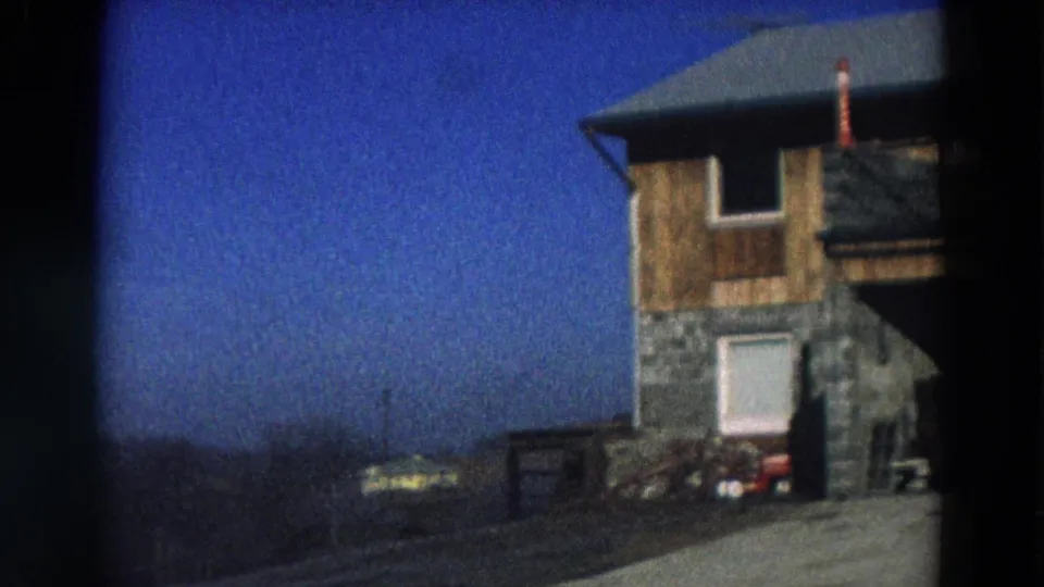 1968 Diller, Nebraska frame with the house cropped at right, driveway and parked cars below, and distant open horizon.