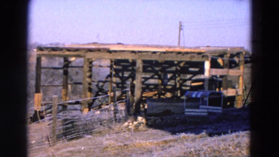 1968 Diller, Nebraska daylight frame showing a wooden shelter, wire fence, dry grass, and a small vehicle near the structure.