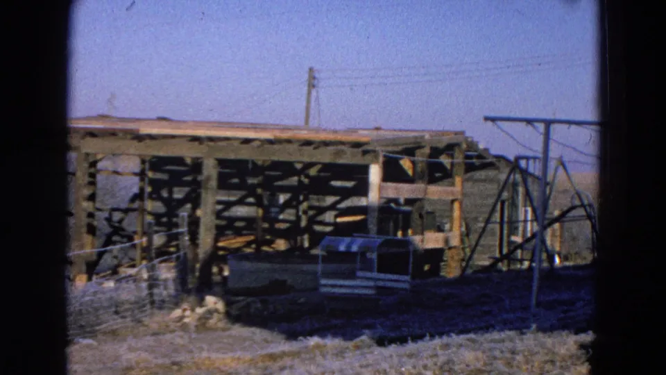 1968 Diller, Nebraska rural yard with an unfinished wooden outbuilding, small animal shelter, fencing, power lines, and a metal frame at right.