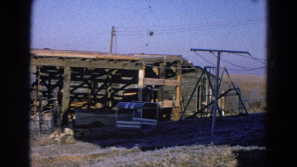 1968 Diller, Nebraska view of a rural wooden structure under construction with fencing, an animal shelter, power lines, and a metal frame nearby.