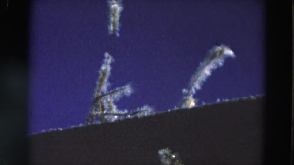 1968 Diller, Nebraska home-movie frame showing blue sky, a dark roof or foreground edge, and pale branch-like shapes near the top.