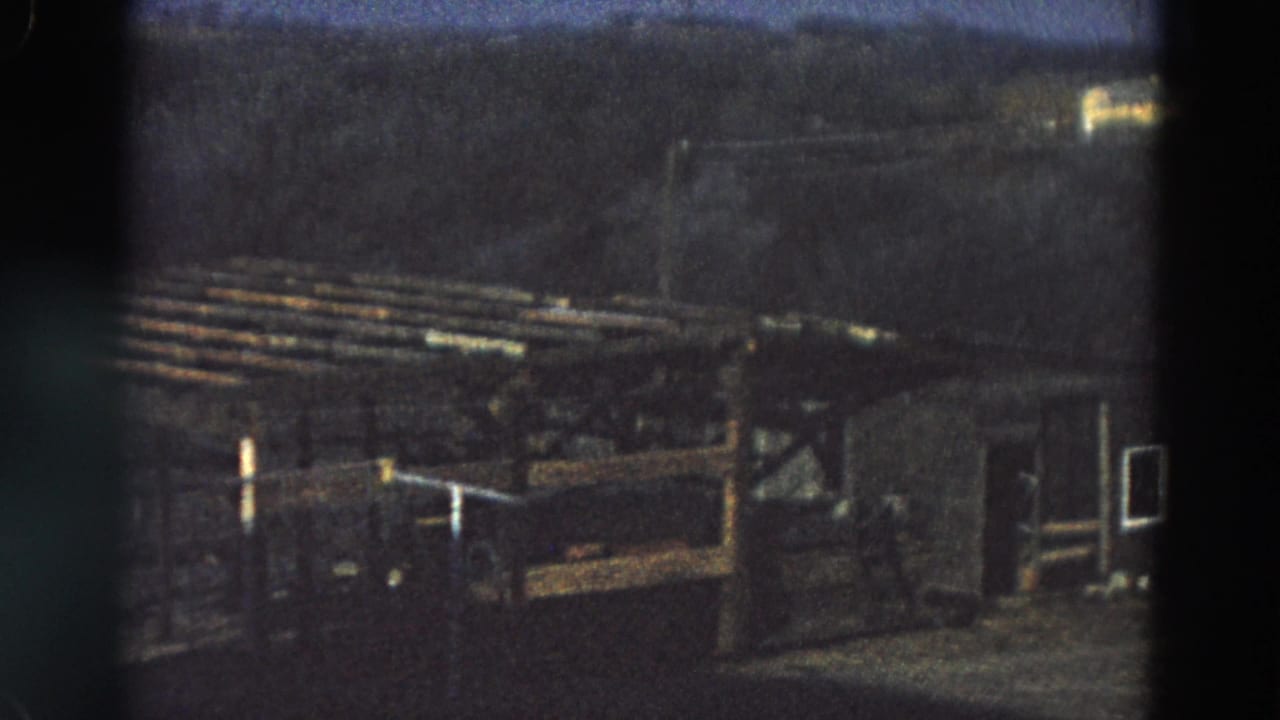 1968 Diller, Nebraska frame showing a weathered brown wooden shelter or pen with slatted rails against a dark treeline.