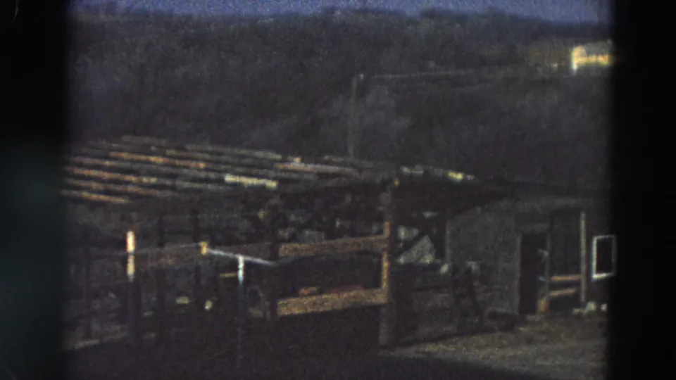 1968 Diller, Nebraska frame showing a weathered brown wooden shelter or pen with slatted rails against a dark treeline.