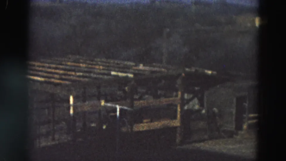 1968 Diller, Nebraska home-movie frame with slatted wood, low framing, and shadowed ground in a rural outdoor setting.