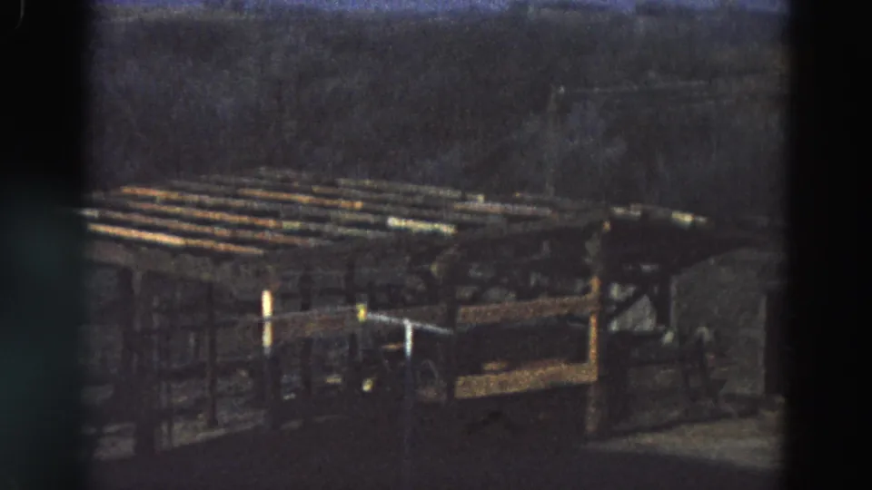 1968 Diller, Nebraska frame showing a rustic brown wooden shelter or pen, horizontal rails, and dark trees beyond.