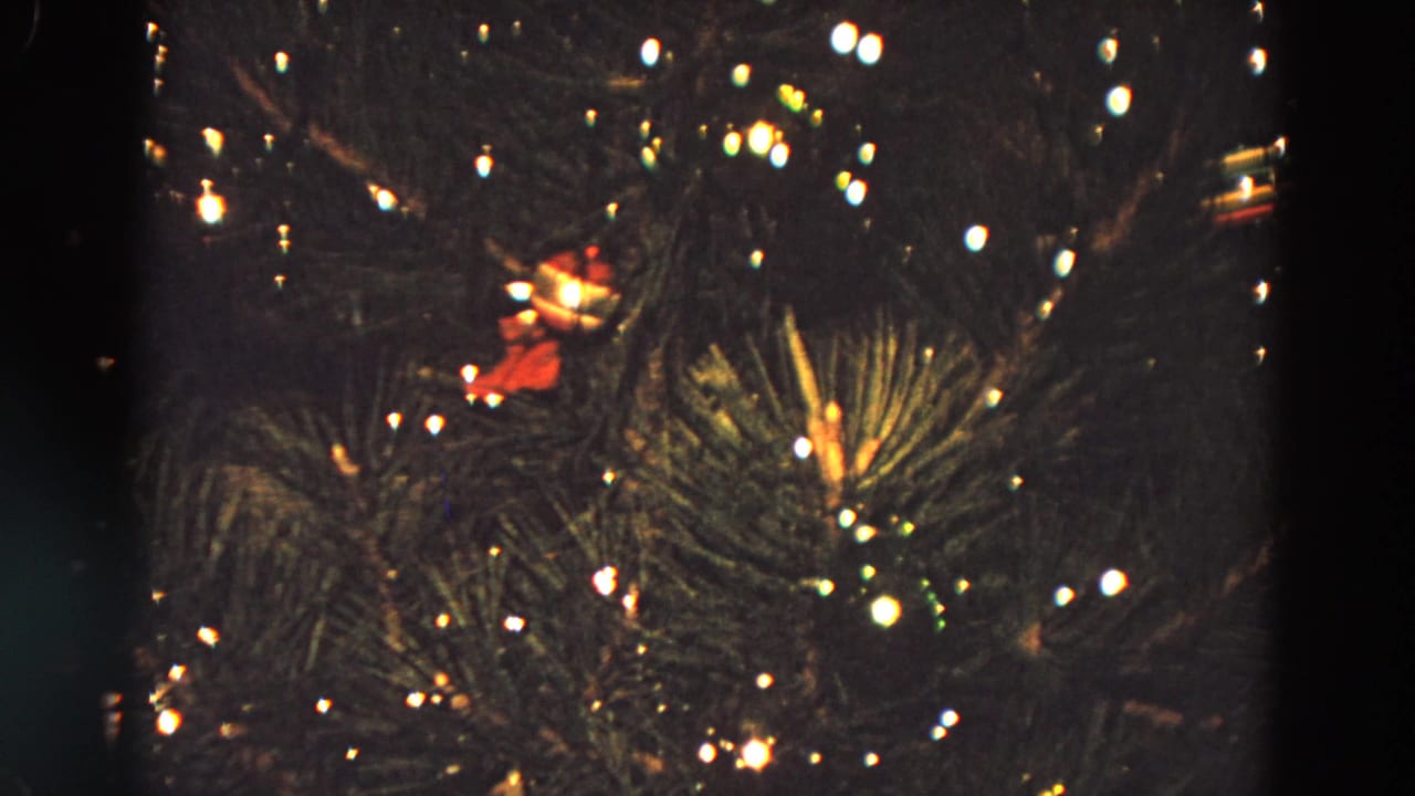 Close view of a lit Christmas tree with ornaments in a dark room.