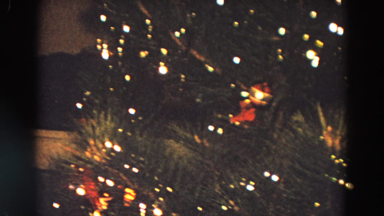 Lit Christmas tree branches with ornaments and a dark vertical film edge.