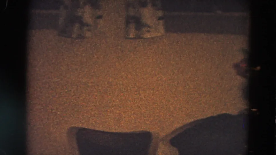 Dim 1968 home-movie frame showing carpet, curtains, and the lower edge of a Christmas tree in an interior room.
