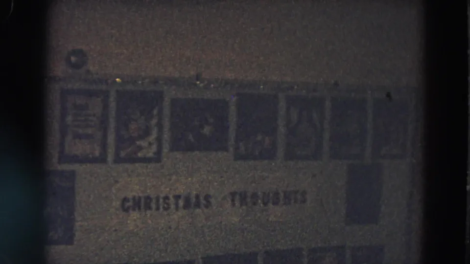 1968 home-movie frame showing a framed holiday display with small pictures and the text CHRISTMAS THOUGHTS on a dim wall.