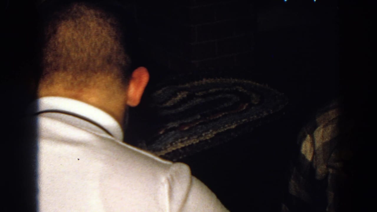 Man in a white collared shirt seen from behind in a dark interior.