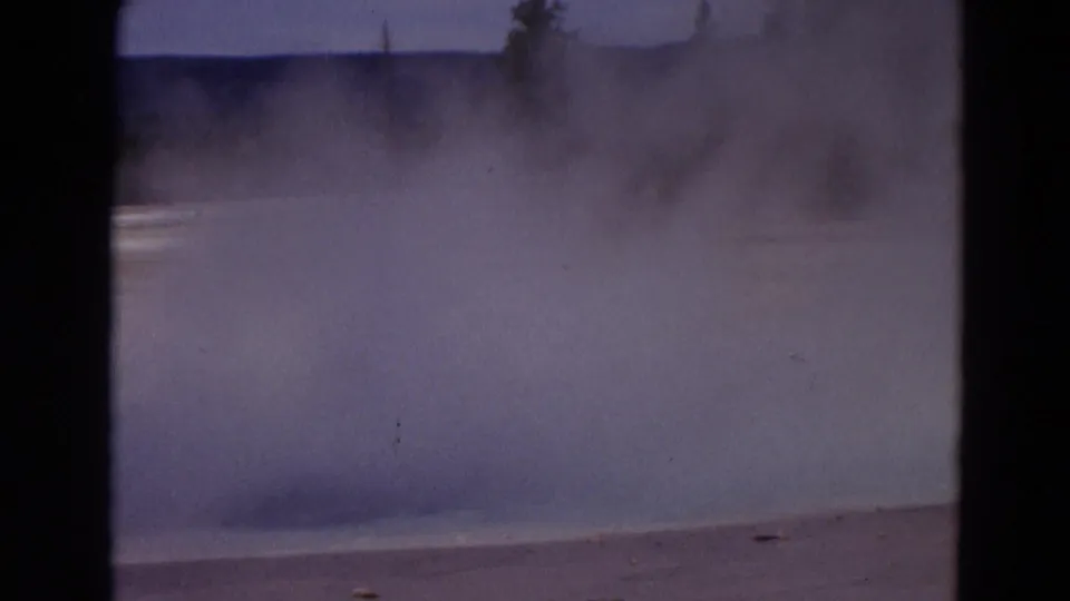 1967 Yellowstone home-movie frame with heavy steam drifting through the Old Faithful area and partly obscuring the landscape.