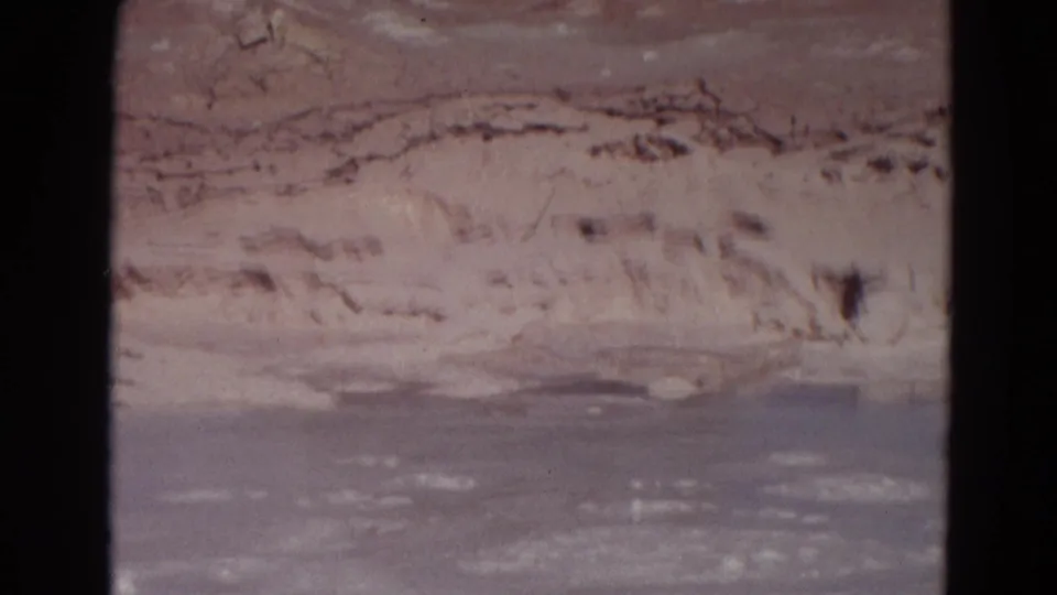 1967 Yellowstone home-movie frame showing a pale mineral edge and gray-blue geothermal water or mud in soft 8mm color.