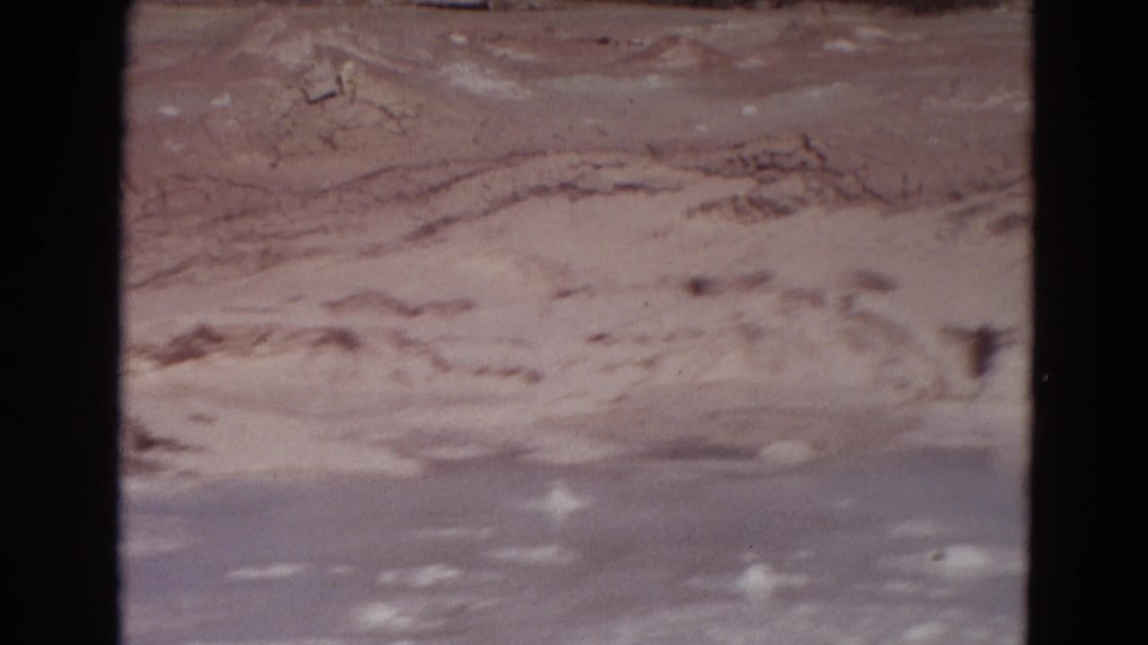 Steaming mineral edge and gray-blue geothermal surface framed by dark film borders.