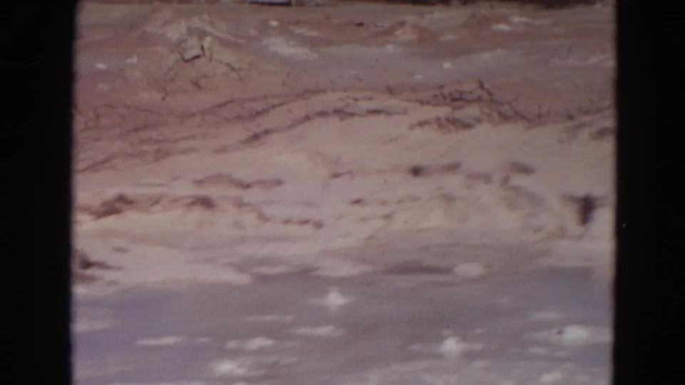 1967 Yellowstone frame with pale mineral deposits and a hazy geothermal surface, viewed from a visitor-shot 8mm perspective.
