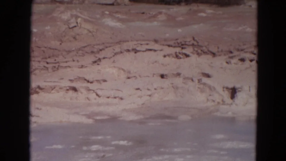 1967 Yellowstone home-movie view of a pale mineral slope and gray geothermal water, with visible grain and soft exposure.