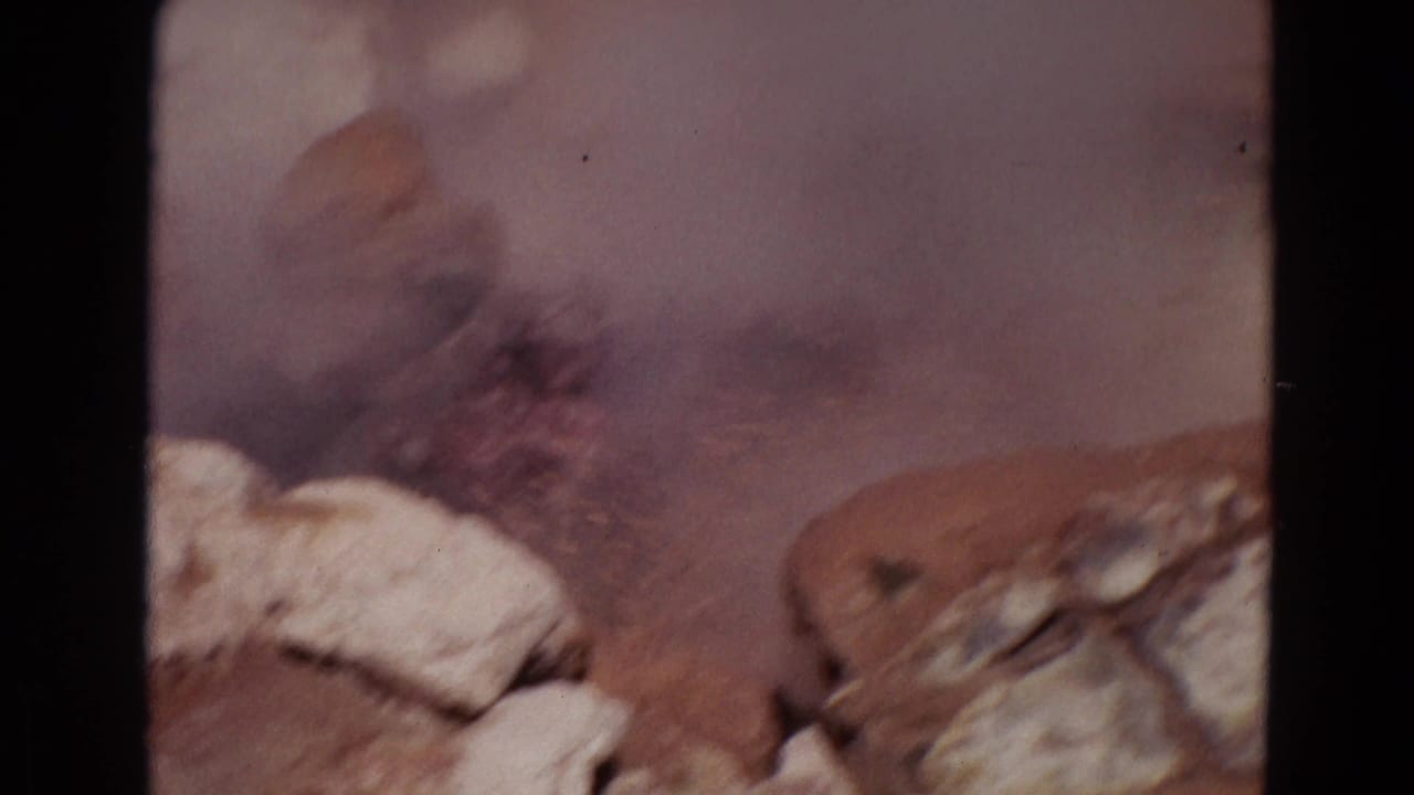 Steam and muddy spray rise behind pale rocks within dark 8mm frame borders.