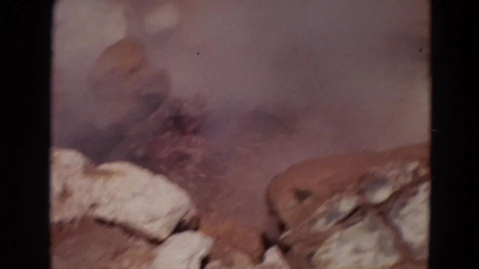 1967 Yellowstone 8mm frame showing steam and muddy water erupting behind pale rocks, with soft focus and visible film edges.