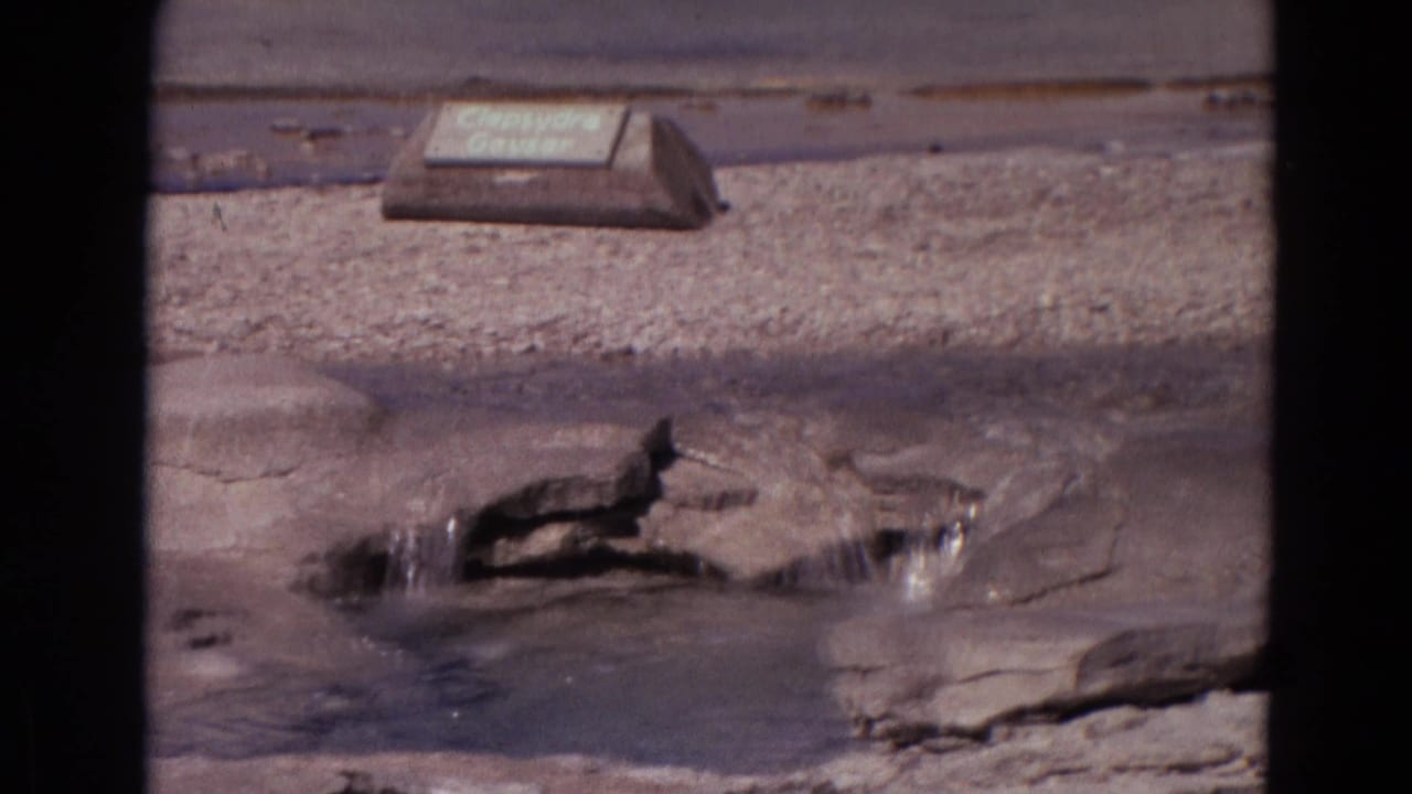 Clepsydra Geyser in Yellowstone appears in a 1967 8mm frame, with water gushing from rock and the identification sign nearby.