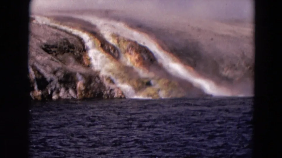 1967 8mm Yellowstone footage shows steam and pale mineral-rich runoff descending a rocky, orange-stained slope into dark water.