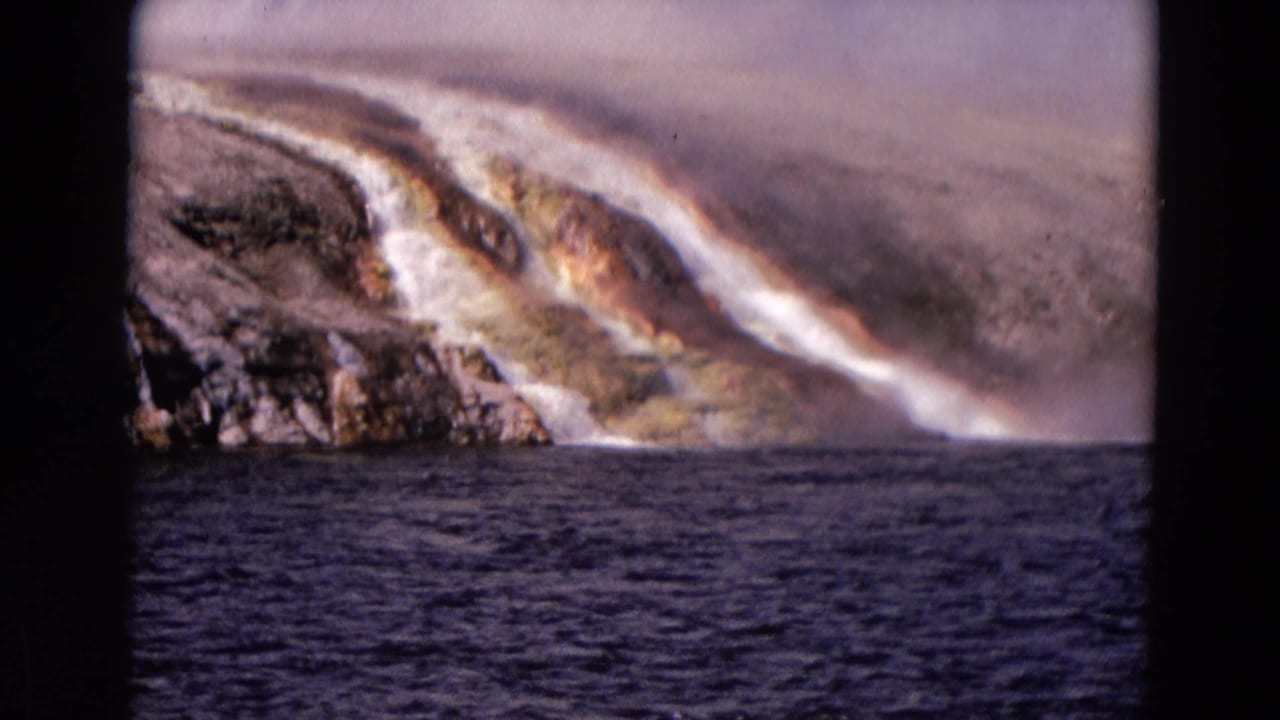 A steaming mineral slope with orange staining sits above rippled dark water.