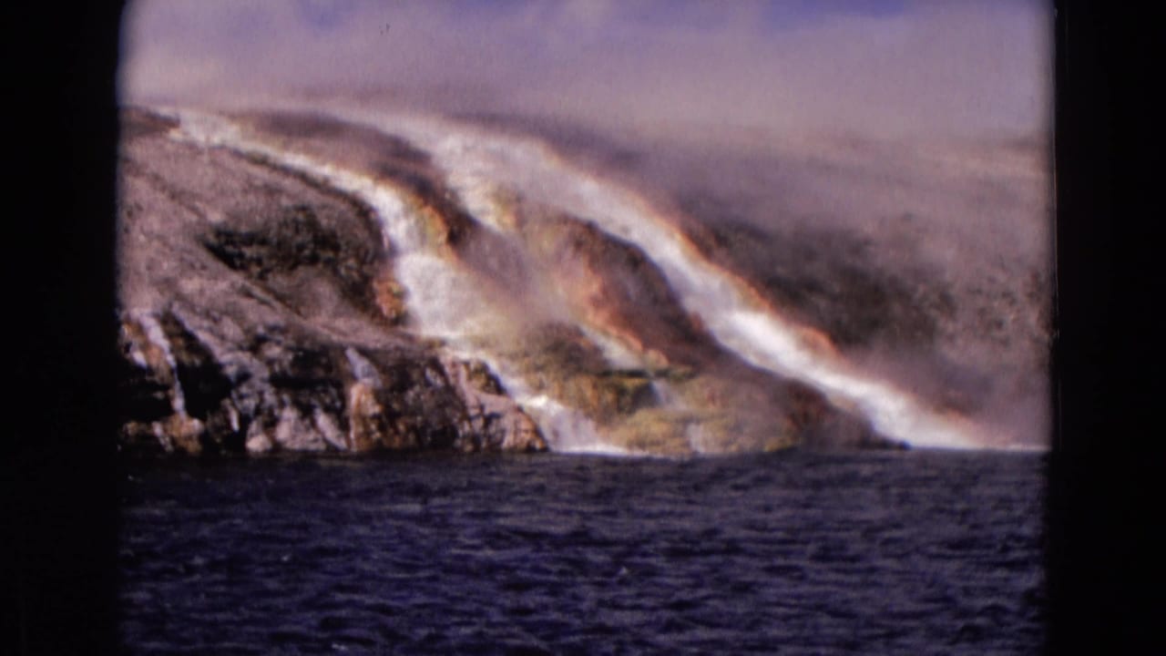 Rushing river below pale rocky banks with mist and a faint rainbow.