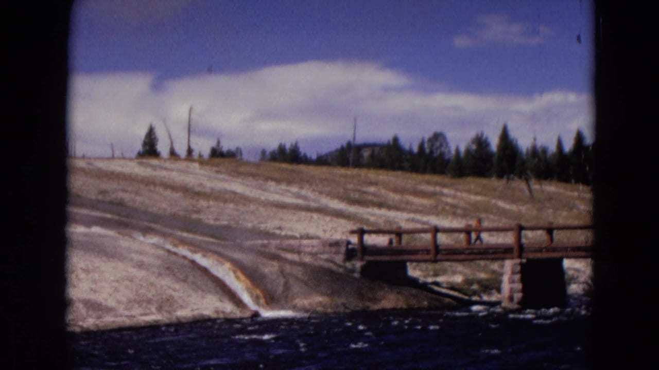 1967 Yellowstone frame with a wooden bridge over water and a small distant person on or near the bridge.