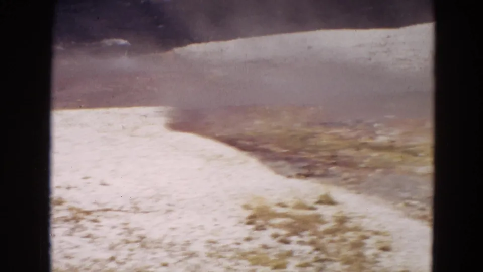 1967 Yellowstone 8mm frame showing a bright mineral terrace and steam over brown, open geothermal terrain.