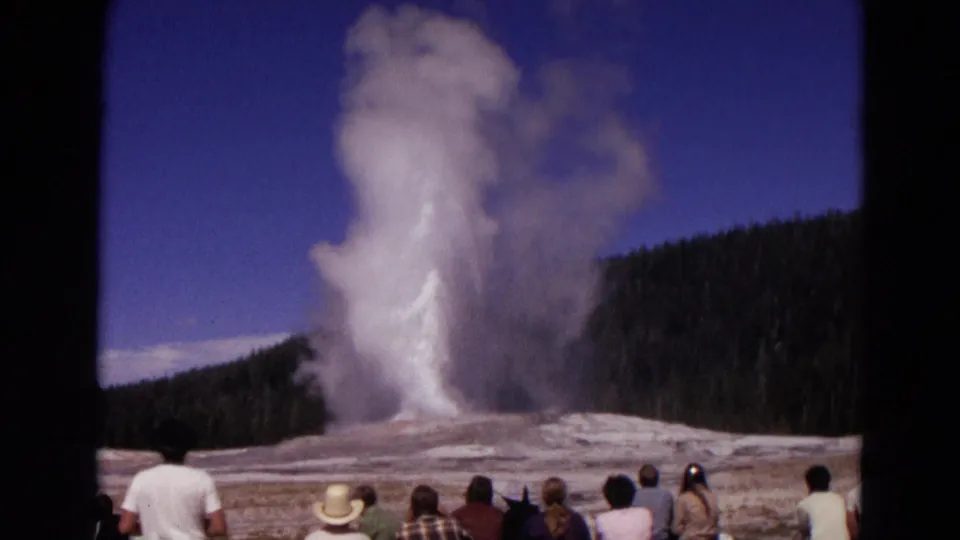 Visitors in casual 1960s clothing watch Old Faithful erupt across the Yellowstone geyser basin.