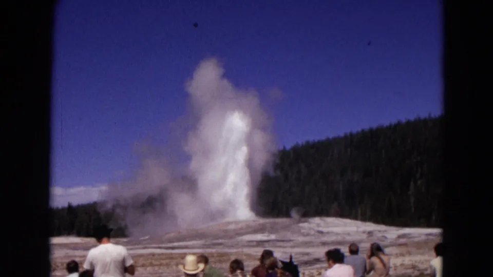 A later moment of the Yellowstone geyser eruption shows water and steam rising while tourists watch from the basin edge.