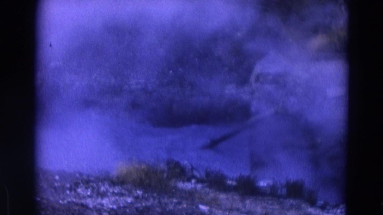 Pale smoke or steam rising from rocky ground with sparse grass and purple film tint.