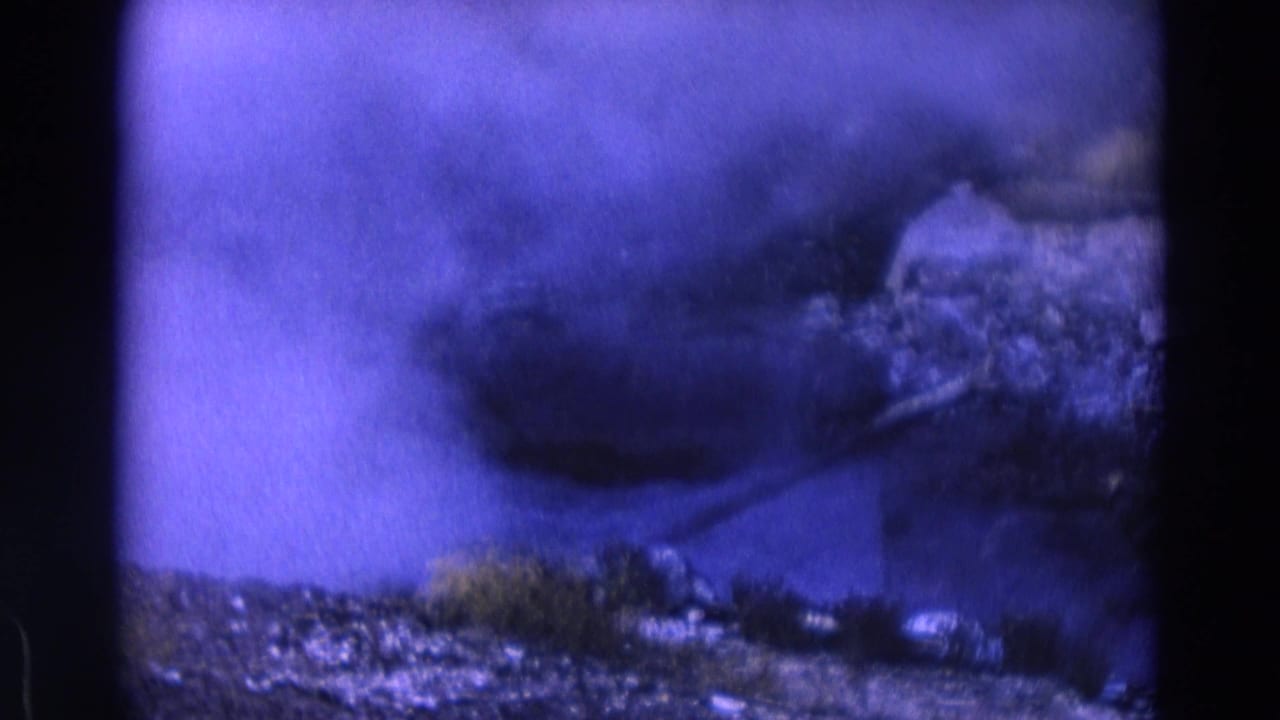 Dense smoke or steam plume moving across rocks and low vegetation.